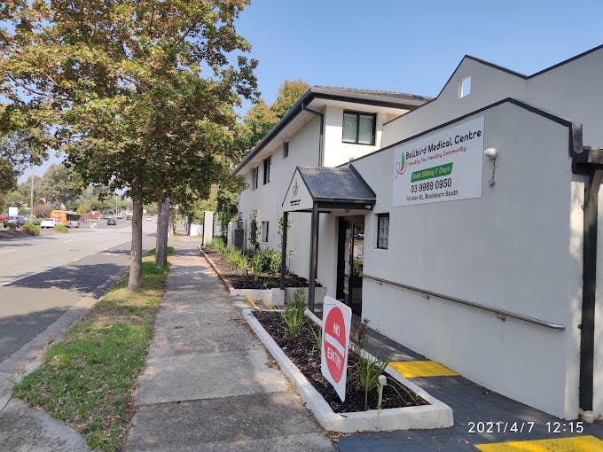 The white weatherboard exterior of Bellbird Medical Centre on Alan Street, with a large sign showing the practice name and phone number, viewed from the tree-lined footpath.