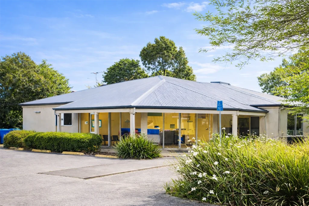 The single-storey brick exterior of Cranbourne East Family Clinic, with a tiled roof, yellow window awnings and garden beds along the front entrance.
